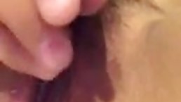 Asian girl is gently stimulating her hairy pussy with her moistened fingers, in front of the camera