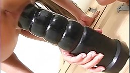 Slim brunette is drilling her pussy with a huge, black dildo, in front of the camera