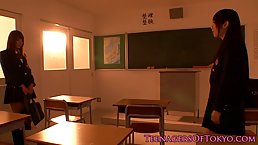 Two Asian schoolgirls are cuddling each other’s nice tits, while in front of the black board