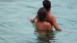 Lovely lady is pressing her natural boobs against her boyfriend's back, while they are in the sea