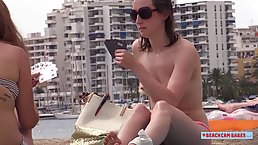 Topless girls are playing cards on the beach, knowing that people are staring at them