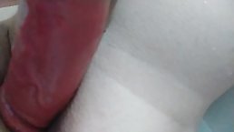 Busty girl is stimulating her shaved pussy with a fake dick, while having a bath