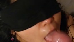 Blindfolded brunette in black fishnets is kneeling in front of her lover while sucking his cock