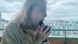 Amateur blonde girl fucks herself with black dildo at balcony